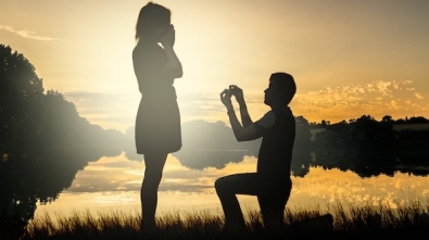 Wedding proposal concept. Young couple have dating at sun set. Man in love is kneeling on knees and giving wedding ring to surprised woman.