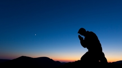 Man praying on the summit of a mountain at sun set with the moon in the sky.