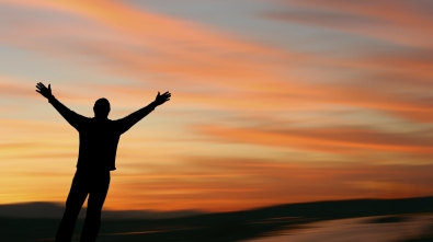 Man with outstretched arms facing a beautiful sunset.