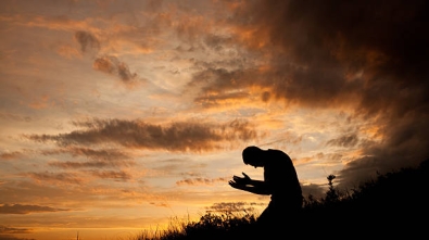 A silhouette of a man praying in a meadow.