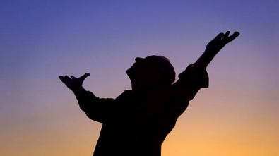 Man standing at sunset with arms open and looking to the sky.