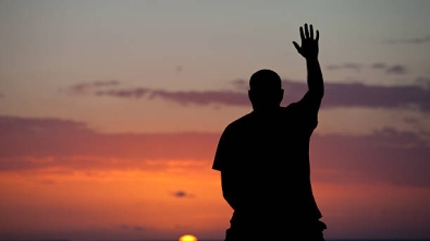 A man lifts his hand towards heaven. Silhouette, rear view, unrecognizable person. A middle-aged man - back view - lifts a hand toward heaven as the sun sets on the ocean. This is a religious themed image. Image location is Central America. Only one person is in the horizontal image.